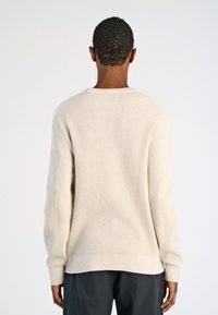 Beige ribbeltrui met lange mouwen en een ronde halslijn. Het materiaal lijkt zacht met een gestructureerd oppervlak en een rechte zoom.