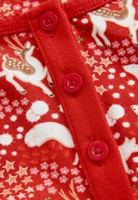 Červená látka s bielymi jeleňmi, hviezdami a kvetinovými vzormi; má červené gombíky na zapínaní; mäkká textúra.