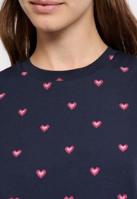 Námořnická bavlněná trička s kulatým výstřihem a roztroušenými růžovými srdíčky. Hladká textura s uvolněným střihem.
