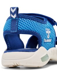 Niebieskie sandały z siatki, z regulowanym paskiem, wyściełaną podeszwą i białymi akcentami. Teksturowany materiał z wentylowanym wzorem i pętelką na pięcie.