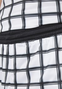 Tessuto a quadri in bianco e nero con motivo a scacchi, dotato di una fascia in vita nera arricciata. Texture liscia con un drappeggio morbido.