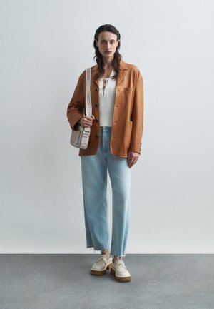Blazer couleur rouille, haut blanc à côtes, jean large bleu clair et chaussures à plateforme crème. Les accessoires comprennent un petit sac avec une sangle à logo.