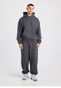 Pullover hoodie en joggingbroek set in donkergrijs. Zachte stof, losse pasvorm, frontzak, elastische manchetten aan de broek, gecombineerd met witte sneakers.