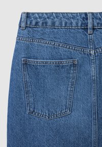 Jeans en denim bleu moyen avec une surface texturée. Comprend une poche arrière avec des coutures renforcées et une taille avec passants de ceinture.