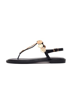 Czarna płaska sandałka z cienkimi paskami, złotymi dekoracyjnymi medalionami na przednim pasku oraz regulowanym zapięciem na kostce.