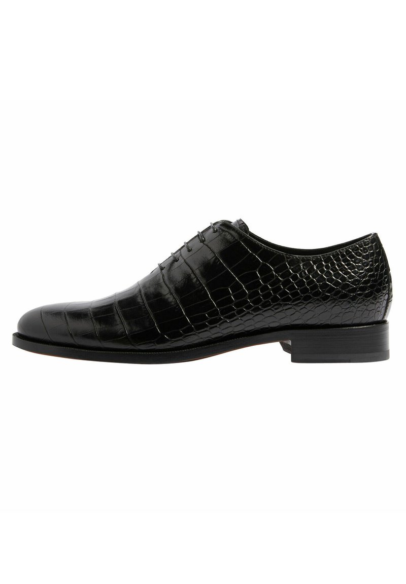 Zapato de cuero negro con un acabado brillante, que presenta un patrón de cocodrilo, punta redonda y un diseño de cordones con cinco ojetes. Tacón plano.