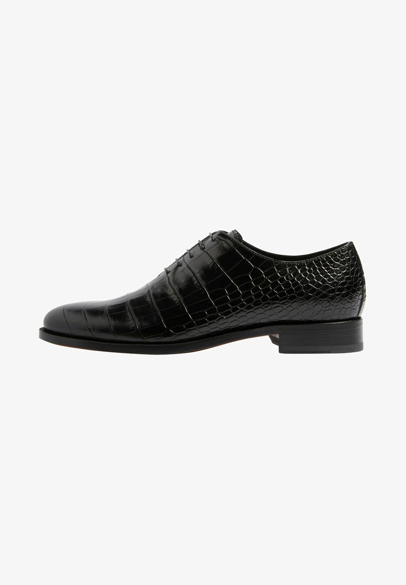 Zapato de cuero negro con un acabado brillante, que presenta un patrón de cocodrilo, punta redonda y un diseño de cordones con cinco ojetes. Tacón plano.