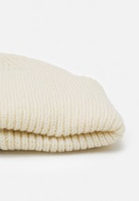 Cream knit beanie with a soft texture, featuring a ribbed pattern and a folded cuff for a snug fit.