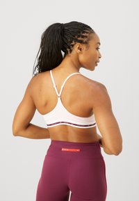 Sostén deportivo en rosa claro con una banda estampada que presenta acentos de logotipo; combinado con leggings burdeos de cintura alta. Tirantes ajustables.