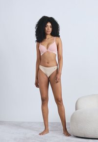 Lyserød polstret bh med justerbare stropper og blondepynt, kombineret med beige bikinitrusser med lav talje; stoffet fremstår glat og elastisk.