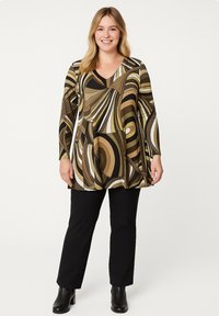 Langsleeve tuniek in abstracte bruine, zwarte en crèmekleurige spiraalpatronen met een V-halslijn. G gedragen met zwarte broeken en enkelboots.