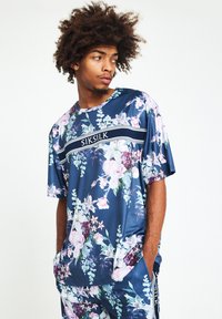 Blommönstrad kortärmad skjorta i marinblå satängtyg. Har ett kontrasterande vitt horisontellt rand med "SIKSILK"-logotyp.