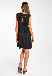 Robe noire avec un corsage ajusté, des manches à volants et une ouverture en forme de trou de serrure dans le dos. Fabriquée en tissu léger avec une jupe fluide.