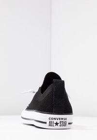 Černé plátěné slip-on tenisky s bílou gumovou podrážkou, s texturovaným svrškem, černým patním jazykem a výrazným logem Converse All Star.