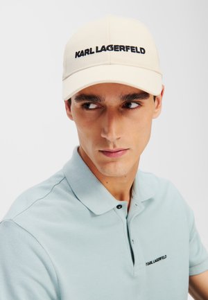 Căciulă de baseball bej cu "KARL LAGERFELD" brodat în negru, fabricată dintr-un material cu un design structurat; purtată de un model într-un tricou polo bleu deschis.