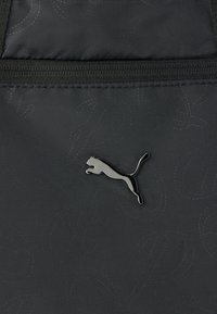 Silver Puma logo on a black quilted fabric surface with visible stitching and a zipper at the top.