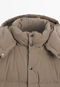 Giubbotto imbottito di un marrone terra con colletto alto. Presenta una texture trapuntata e bottoni a pressione metallici lungo la parte anteriore.