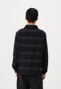 Black and gray flannel shirt with a plaid pattern, buttoned collar, long sleeves, and a relaxed fit, shown from the back.