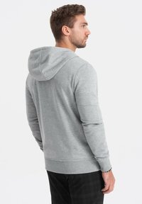Grauer Kapuzenpulli mit Kordelzug, langen Ärmeln, gerippten Bündchen und Saum. Glatte Textur, lässiges Design, von hinten betrachtet.