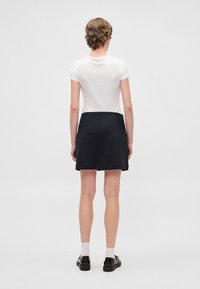 Wit T-shirt met korte mouwen gecombineerd met een donkerblauwe A-lijnrok. Gladde textuur en eenvoudig ontwerp; minimale details. Zwarte schoenen en witte sokken.