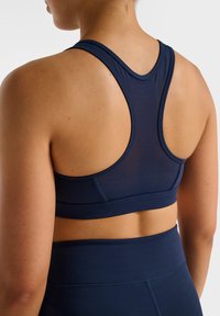Mörkblå sport-bh med racerback-design, tillverkad av slätt tyg. Syftesfulla detaljer inkluderar sömlös finish och ett stödjande band.