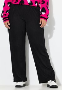Pantaloni neri a gamba larga con motivo a onda testurizzato, vita elasticizzata e vestibilità rilassata, abbinati a scarpe bianche.