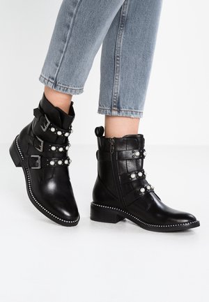 Bottes noires en cuir à la cheville avec trois sangles décoratives ornées de boucles argentées et de fausses perles, fermeture éclair, et semelle texturée avec surpiqûres.