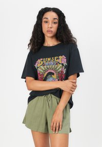 T-shirt graphique noir avec un design coloré "Sunset Roxy", associé à un short léger vert avec cordon de serrage. Coupe décontractée, manches courtes.