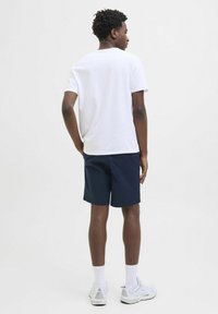 Hvid bomulds t-shirt, marineblå shorts, hvide sportsko og hvide sokker. Kortærmet, afslappet pasform, minimal branding, enkelt design.