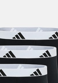 Svarta boxershorts med en vit elastisk midjeband som har svart Adidas-logotyp och ränder. Slät tygtextur, tre par staplade.