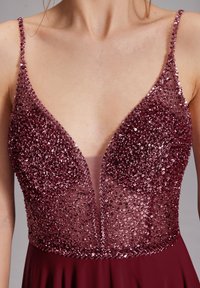 Vestido burdeos oscuro con tirantes finos, con un escote en V pronunciado cubierto de lentejuelas densamente colocadas.