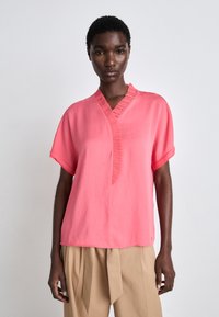 Rosa Kurzarmshirt mit leicht gefälteltem V-Ausschnitt und lockerer Passform. Hergestellt aus einem leichten Stoff mit glatter Textur.