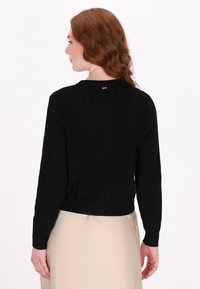 Maglione nero a coste con maniche lunghe e design corto. Presenta un colletto semplice e un logo discreto sul retro.