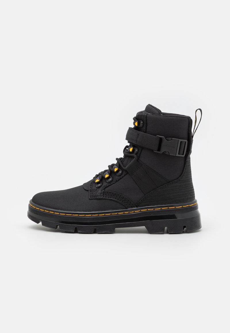Botte montante noire avec semelle épaisse, surpiqûres jaunes, six œillets métalliques avec accents jaunes, bride à la cheville et languette à l'arrière.