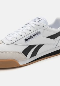 Baskets synthétiques blanches avec accents noirs et logo Reebok. Elles sont dotées d'un système de laçage, d'un empiècement en daim doux sur le bout et d'une semelle en caoutchouc naturel.