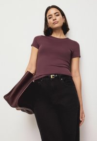 Tumepunane keha järgnev T-särk lühikeste varrukatega, kombineeritud mustade kõrge vöökohaga teksade ja suure veinipunase käsitaskuga. Tekstureeritud kangas, vabaaja disain.