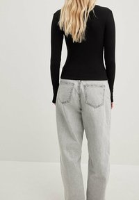 Hladký černý top s dlouhým rukávem, kombinovaný se světle šedými denimovými kalhotami širokého střihu, které mají dvě zadní kapsy a vybledlou texturu.