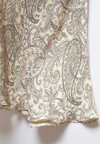 Beige stof med et detaljeret sort paisley-mønster med indviklede svungne former og blomsterdetaljer, der falder blødt ved kanten.