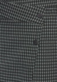 Tessuto a fantasia bianco e nero con una finitura testurizzata, caratterizzato da due bottoni neri e un sottile motivo geometrico su tutta la superficie.