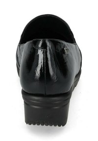 Scarpa in vernice nera con punta arrotondata e suola bassa a piattaforma. Dettagli notevoli includono cuciture sul retro e un piccolo accento metallico.