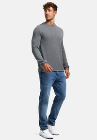 Grå langermet strikket skjorte med ribbet tekstur og rund hals, kombinert med lyseblå denimjeans og hvite sneakers.