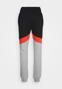 Schwarze und graue Jogginghose mit einem leuchtend roten Abschnitt. Verfügt über einen elastischen Bund, zulaufende Beine und eine Gesäßtasche. Weiches Material aus Baumwollmischung.