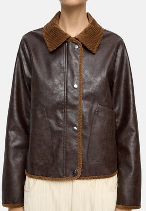 Ciemnobrązowa skórzana kurtka z teksturowanym kołnierzem i wykończeniem z sztruksu, przednie zatrzaski i dwie przednie naszywane kieszenie, noszona na jasnych spodniach.