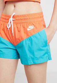 Plavky Nike s oranžovými a tyrkysovými panely. Vyrobeno z lehké látky s elastickým pasem a šňůrkou. Bílý detail loga.