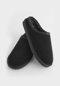 Schwarze Wildlederschuhe mit einem weichen, strukturierten Innenfutter. Rundliche Form mit einer flachen schwarzen Sohle. Keine sichtbaren Muster oder Metallteile.