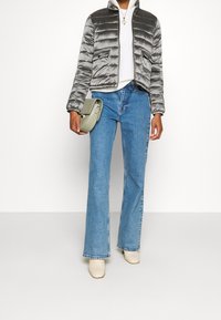 Grå dunjakke med slank pasform, lynlås foran, to lommer, kombineret med lyseblå vide jeans og beige ankelstøvler, holder en grøn håndtaske.