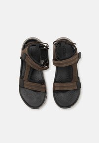 Brune sandaler med justerbare stropper, teksturering på den svarte sålen, og en gummisåle. Har snøring for en sikker passform.