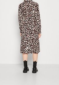 Abito a maniche lunghe di colore nero con stampa leopardata rosa e bianca. Presenta una vita cinturata e una lunghezza midi, abbinato a stivali neri alla caviglia.