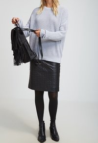 Ljust grått stickat tröja, svart vadderad läderkjol, svarta strumpbyxor, svarta ankelstövlar, håller en svart fransväska.