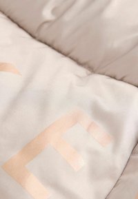 Tela de chaqueta acolchada beige con una textura suave, que presenta sutiles acentos metálicos en un patrón geométrico y un acabado brillante.
